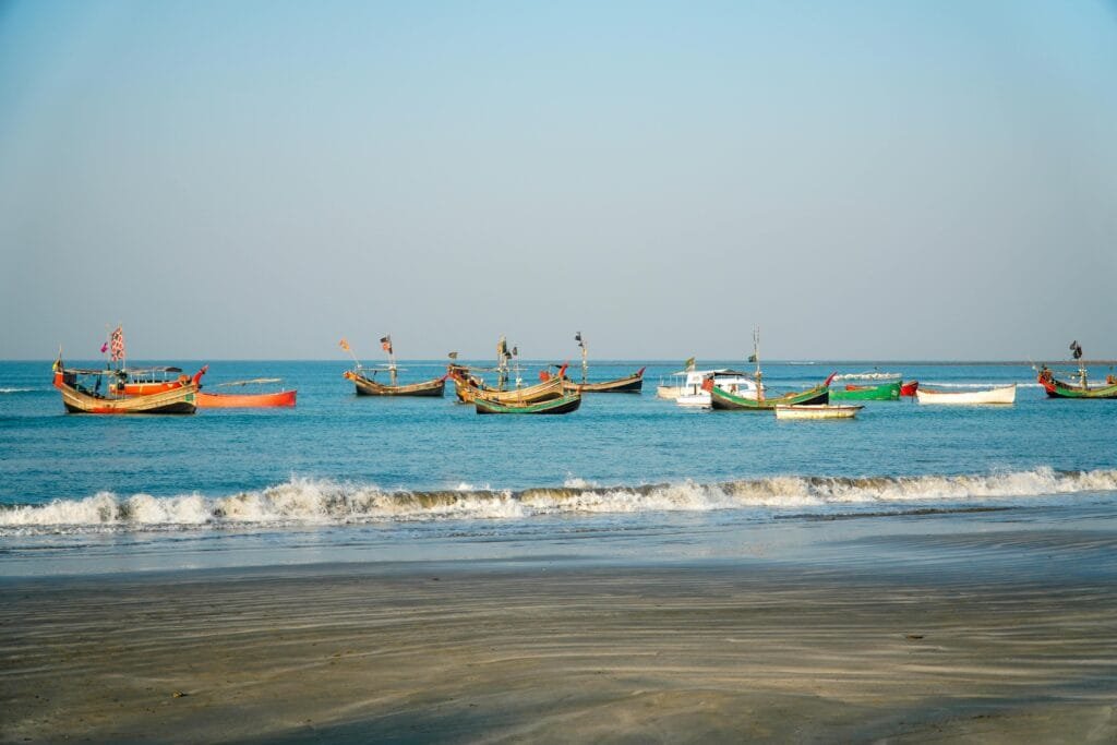 Colorful fishing boats float on calm blue waters near a peaceful tropical beach.